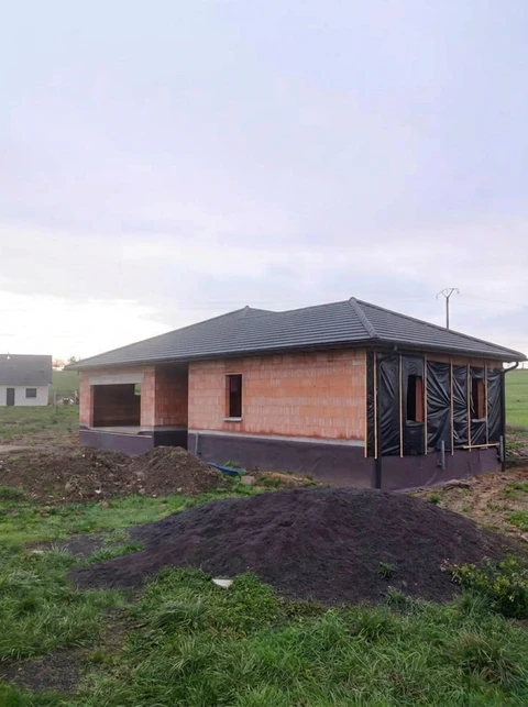 Maison individuelle plain-pied en cours de construction, structure en briques de terre cuite apparentes, toiture en tuiles ardoisées type hip roof (quatre pans)