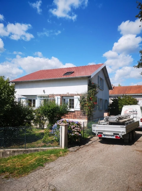 Maison individuelle de style traditionnel français, façade blanche avec volets bleus, toiture en tuiles rouges avec fenêtre de toit type Velux